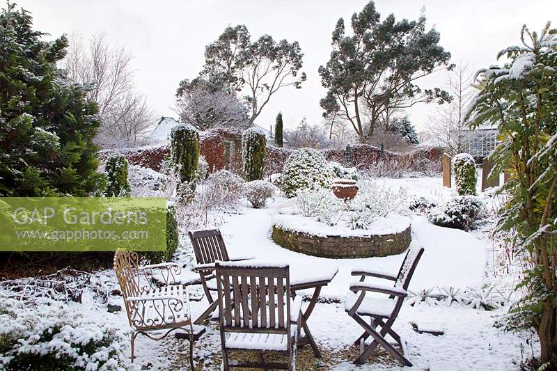 Seating area and raised circular bed in snowy formal garden. 
