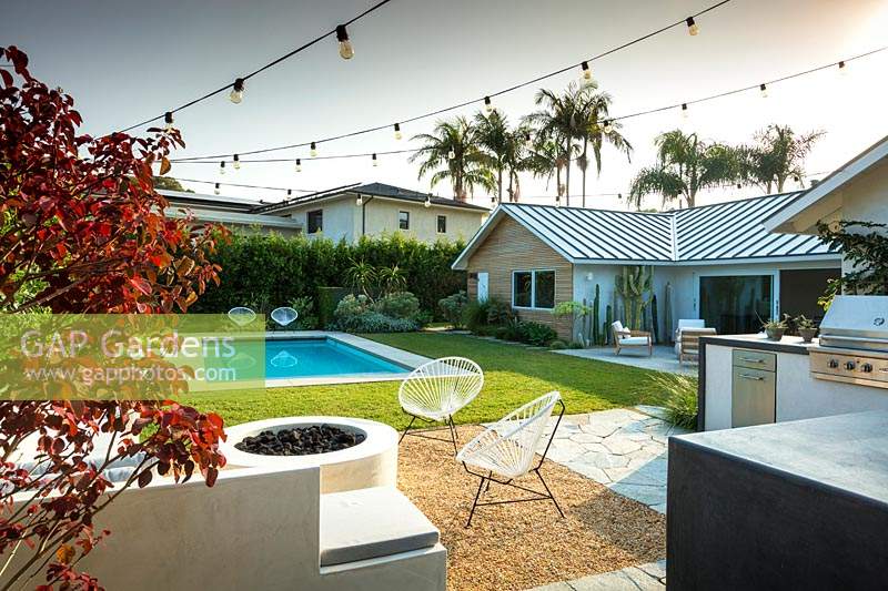 View across garden with carnival string lights to swimming pool and outside seating area. Garden designed by Falling Waters Landscape, inc Ryan Prange, New Port Beach, California, USA.