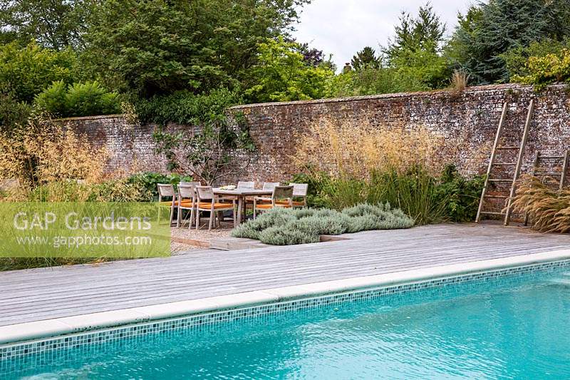 View across the swimming pool to dining area in contemporary country garden near Winchester, Hants., UK. Designed Elks-Smith Garden Design.