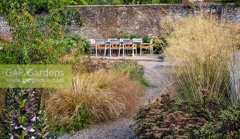 View past mixed perennial and grass border in contemporary garden to dining table and chairs. Designed Elks-Smith Garden Design.