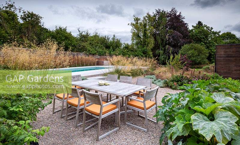 Dining table and chairs with view to swimming pool, in contemporary garden near Winchester, Hants, UK. Designed Elks-Smith Garden Design.