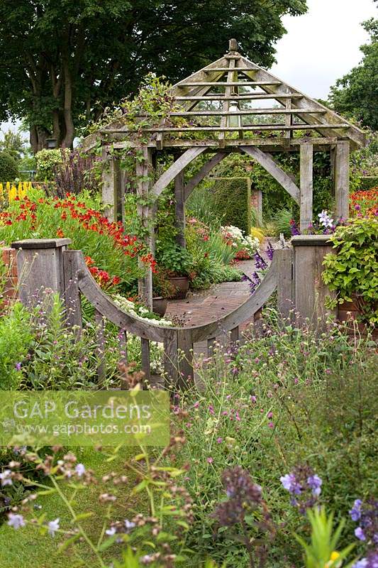 Wooden gateway and pergola surrounded by perennial borders in the Sundial Garden at Wollerton Old Hall Garden, Market Drayton, UK. 