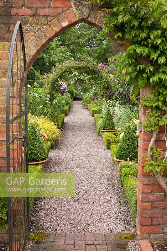 View through brick arch and gateway to Buxus - Box edged borders of the Long Border at Wollerton Old Hall, Shropshire, UK. 