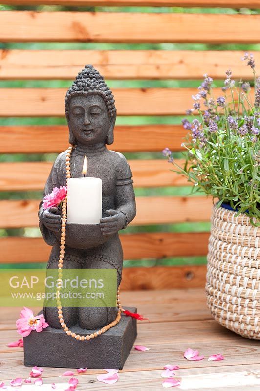 Buddha holding a candle next to a basket of sage on wooden balcony. 