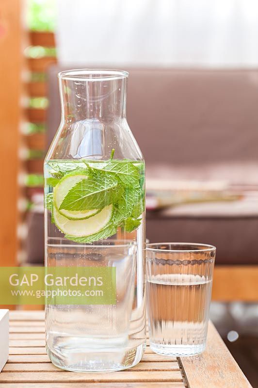 Water carafe with lime and mint and a drinking glass on a table, on mediterranean summer balcony.