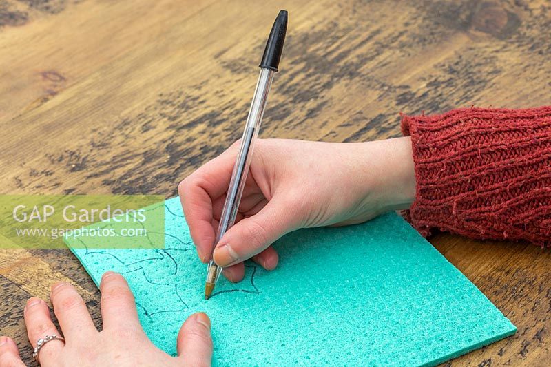 Woman drawing out holly-leaf shapes on green foam.