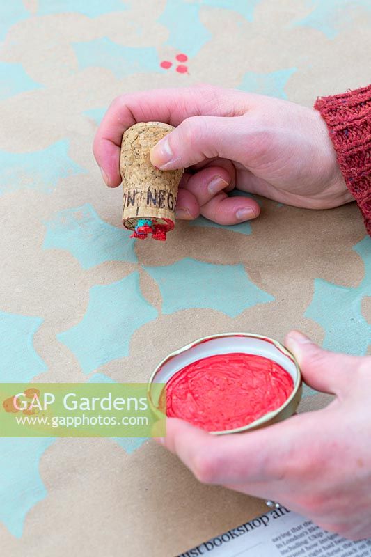 Woman using cork stamp to create holly pattern wrapping paper.