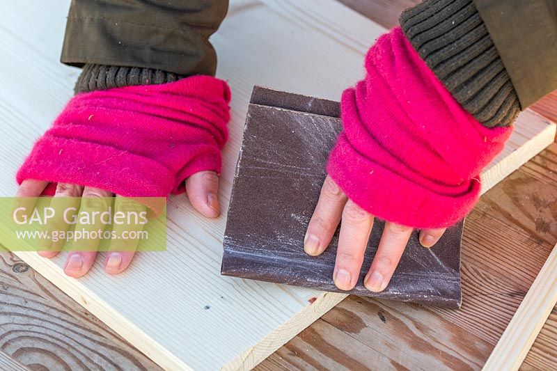 Woman sanding cut edge of piece of wood.