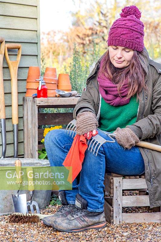 Woman rubbing garden rake with oily rag.