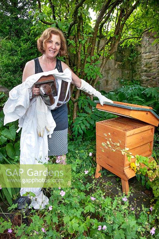 Esther Mendelssohn standing by beehive with beekeepers suit and bee smoker. 