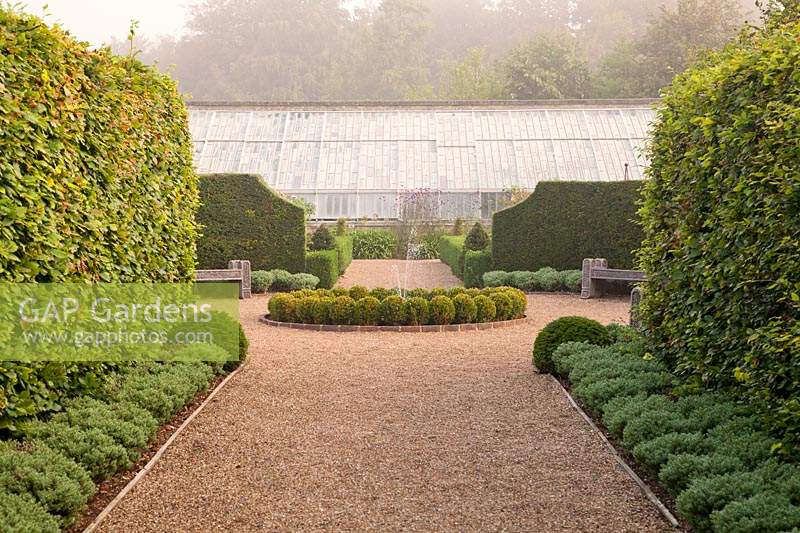 View past clipped topiary hedges to central water feature and fountain and glasshouse beyond. Arundel Castle, Sussex, UK. 

