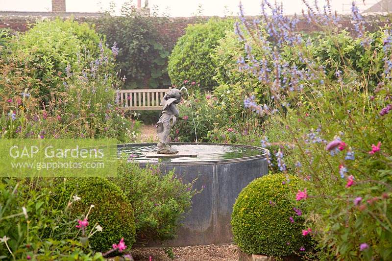 Decorative metal pool and cherub fountain amongst late summer planting, with clipped Buxus balls. Arundel Castle, Sussex, UK. 