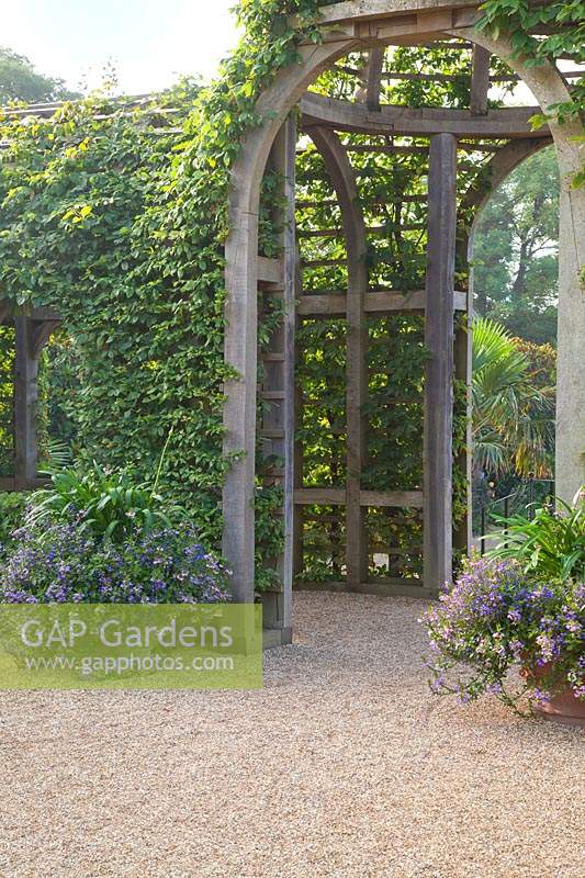 Entrance to wooden arbour in Collector Earl's garden with decorative containers. Arundel Castle, Sussex, UK.