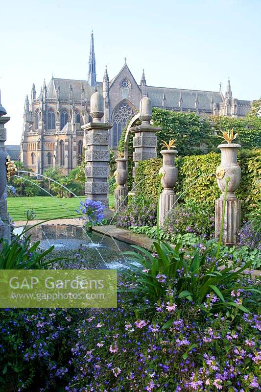 Italianate fountains in Collector Earl's garden, alongside pool with flowering Agapanthus, Lobelia and Scaevola with cathedral beyond. Arundel Castle, Sussex, UK. 