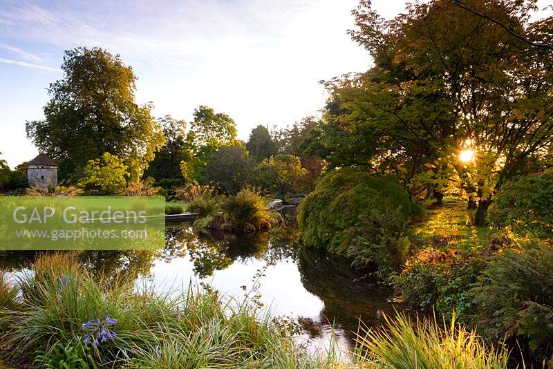 The Lower Pond adjoining the Round Garden is surrounded by trees and shrubs. Llanover Gardens, Monmouthshire, UK. 