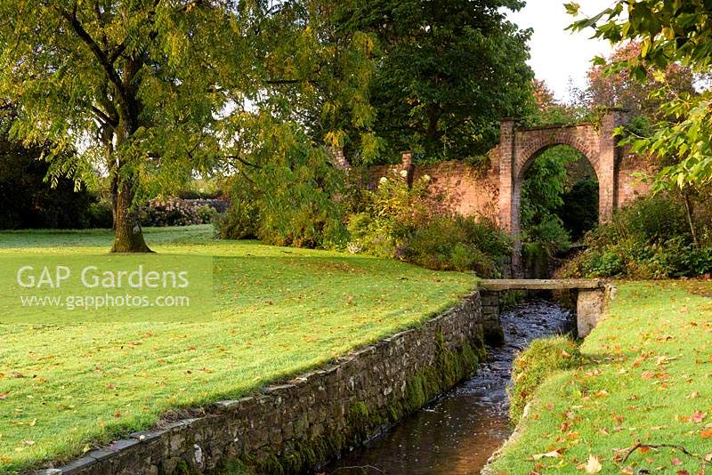 A stream runs through a stone lined channel snaking across the parkland at Llanover Gardens, Monmouthshire, UK.