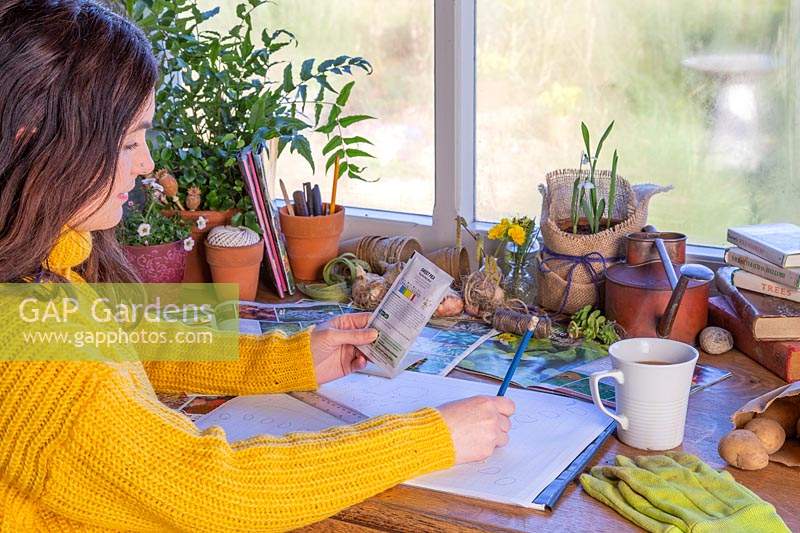 Woman reading back of seed packet at desk.