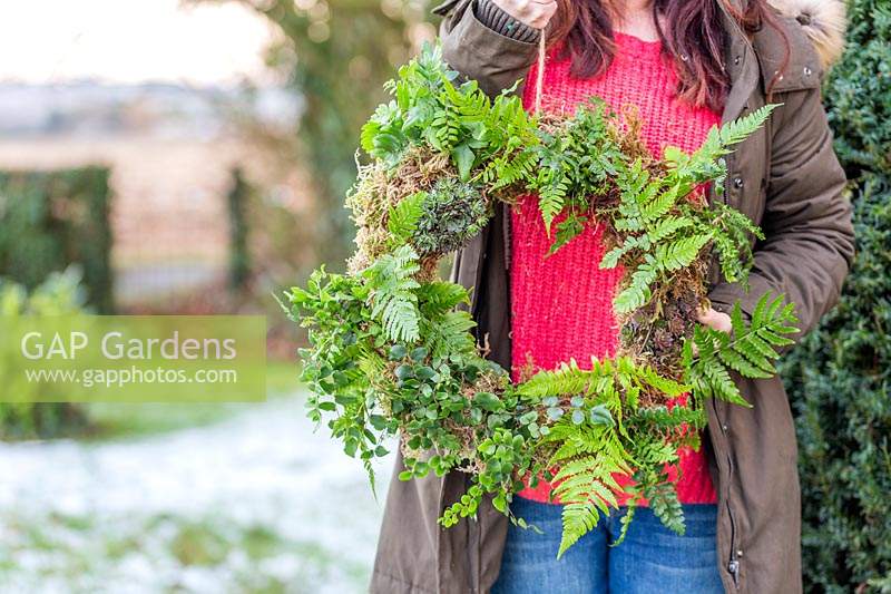 Woman holding up completed moss and fern wreath in snowy garden