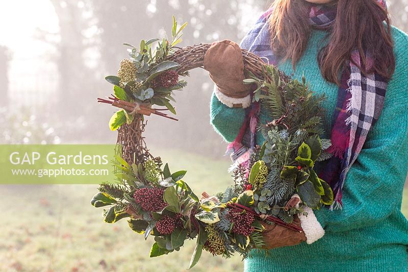 Woman holding finished foraged wreath in misty garden