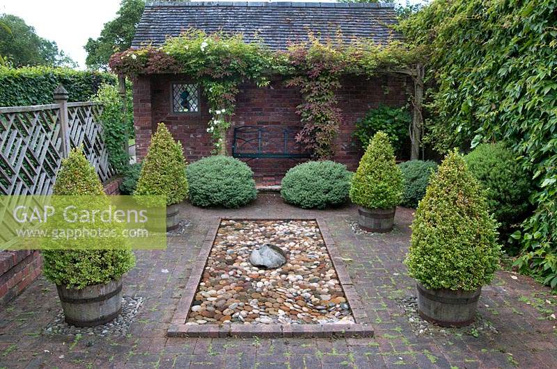 Formal Italian-style paved courtyard with Buxus - box - topiary in containers,
 rectangular pond and Parthenocissus - Virginia creepers climbing over brick 
arbour 