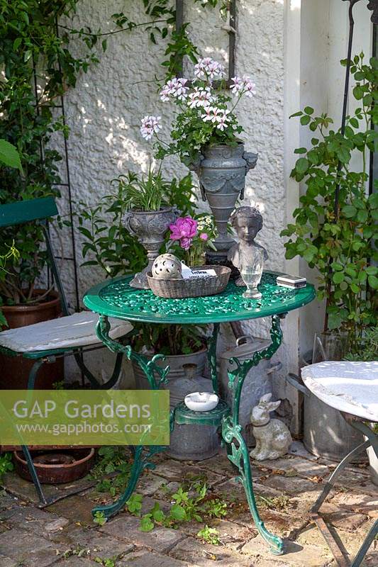 Display of collectables and pot plants on metal table near house 
