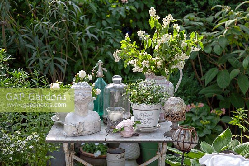 Old decorative objects displayed on vintage table, mostly white items set against greenery in a garden