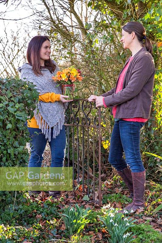 Two women exchanging a gift of a vase of flowers in garden. 