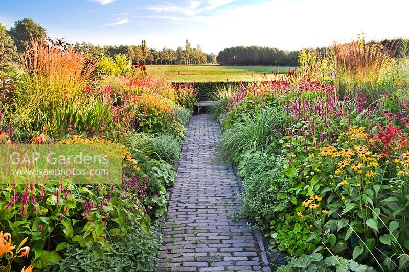 Double herbaceous borders with a paved path leading through to the bench. 