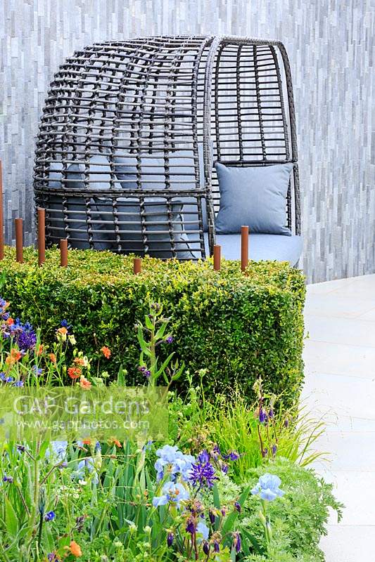 A grey basket-weave seat with grey cushions sits against a wall clad with light and dark grey split-faced porcelain. The Habit of Living â€“ A Garden In Support of Diabetes UK, designed by Karen Tatlow and Katherine Hathaway. RHS Malvern Spring Festival, 2019. 