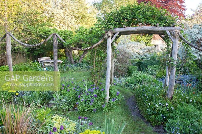 Decorative rope feature and rustic archway dividing garden areas, all underplanted with informal flower beds
