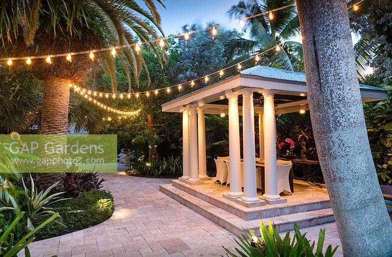 Paved shelter with pillars with furniture and string lighting. The Jones Residence, Key West, Florida, USA. Garden design by Craig Reynolds.