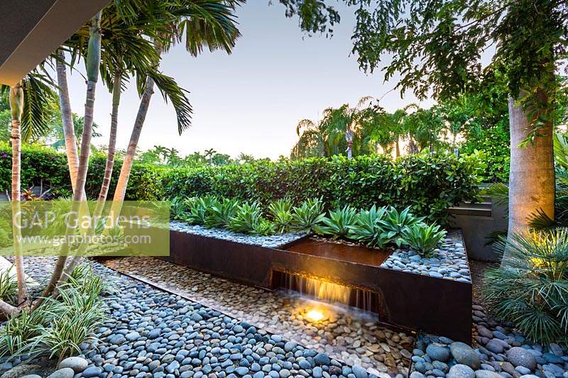 Corten steel water feature with cobbles, waterfall, rill and raised bed with rows of Agave weberi

