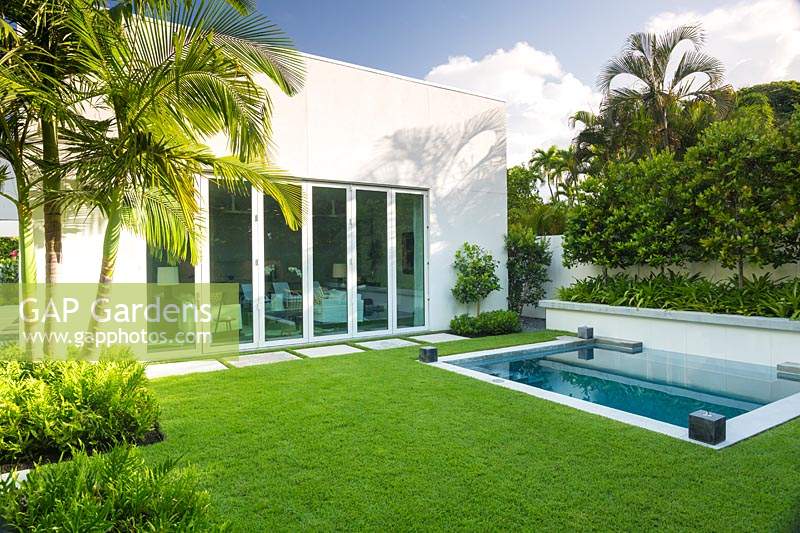 View aross Zoysia grass lawn to back of house with folding doors by swimming pool and raised bed of Citrus - Orange trees