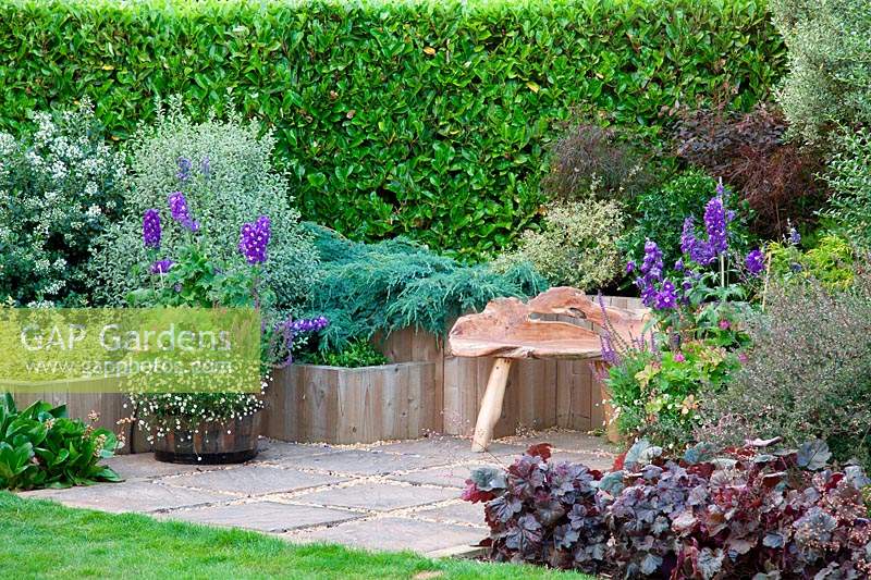 Seating area surrounded by raised beds planted with shrubs and perennials. Designer Karen Tatlow's garden, Lichfield