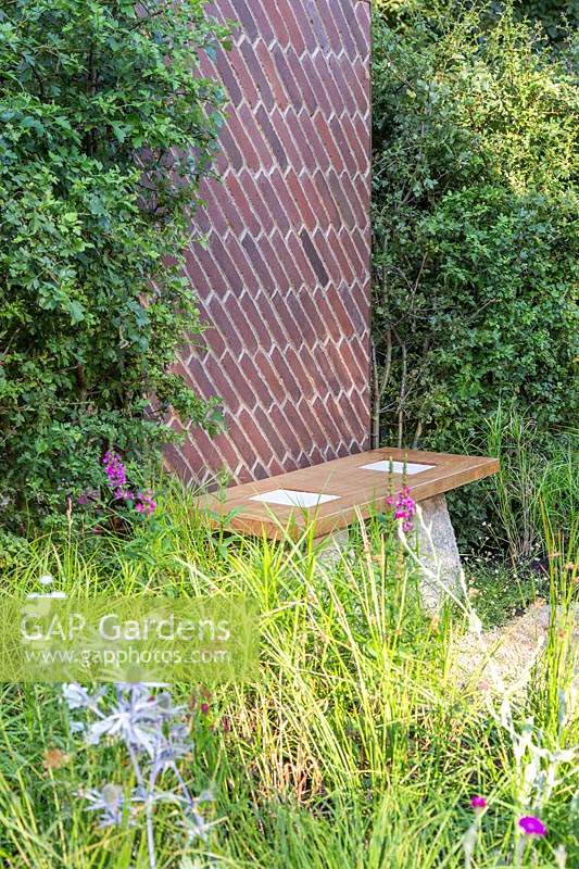 Brick screen between hedging, by a bench of Scottish oak with staddle stones in 
'South Oxfordshire Landscape Garden'