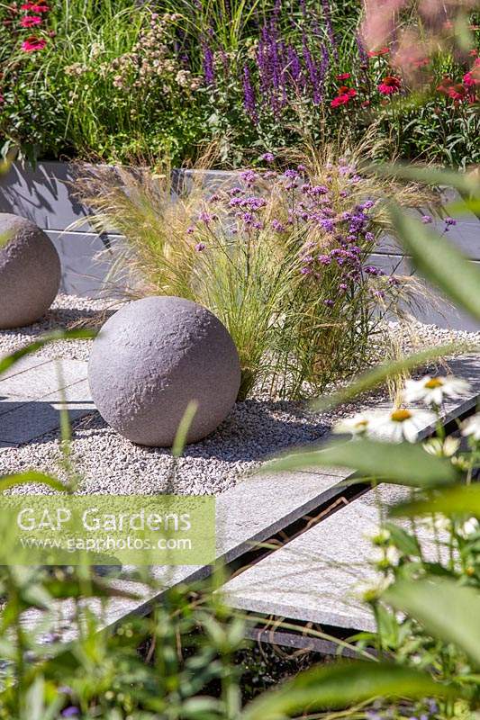 Paving area with paving, chippings, spheres and ornamental grasses in the 
'Secured by Design' garden