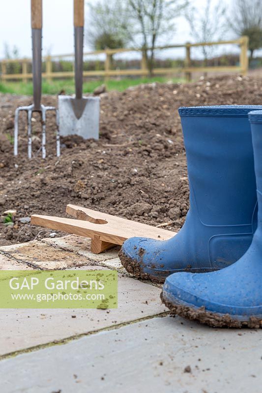 Muddy boots and boot Jack on paving near soil and digging tools