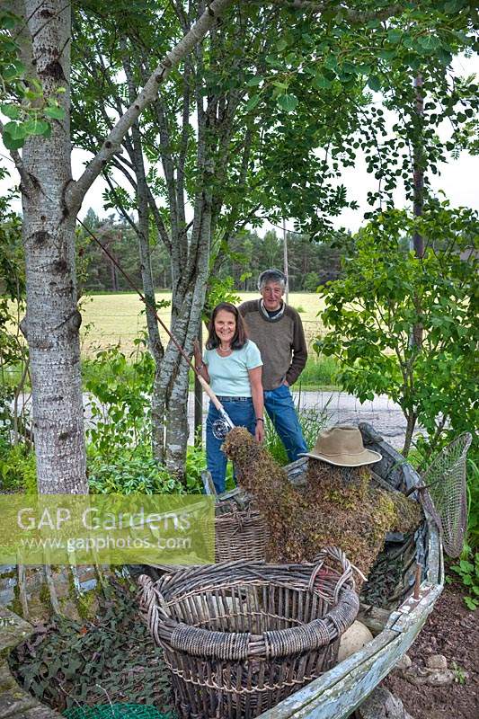 Couple standing by a garden feature comprising figure of fisherman fly fishing inside an old rowing boat