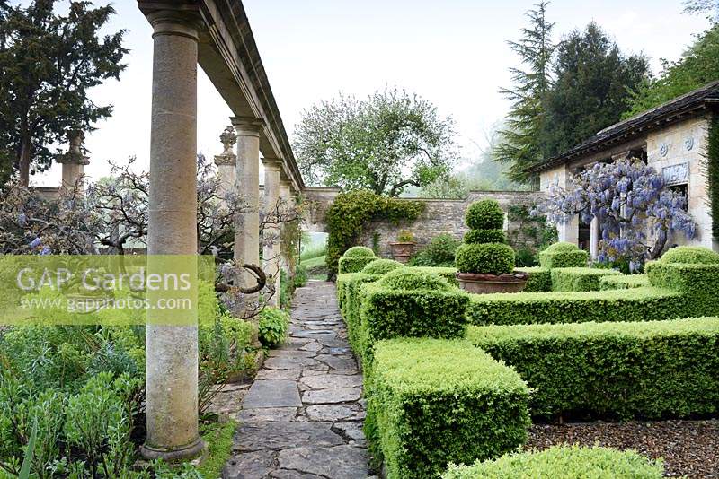 The Casita with wisteria, clipped box parterre and colonnade on the Great Terrace at Iford Manor, Bradford-on-Avon, Wiltshire, UK. 