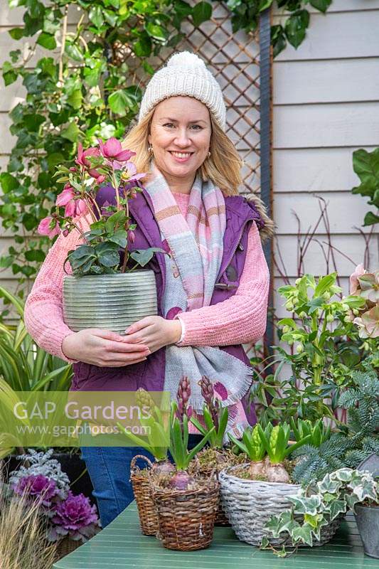 Woman holding pot of pink hellebore in early-spring courtyard setting.