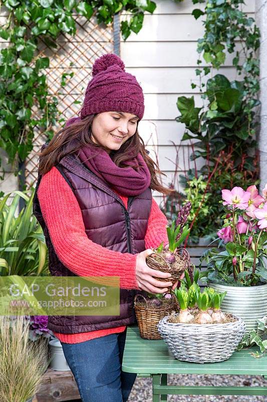 Woman holding basket with Hyacinthus in early-spring courtyard setting.