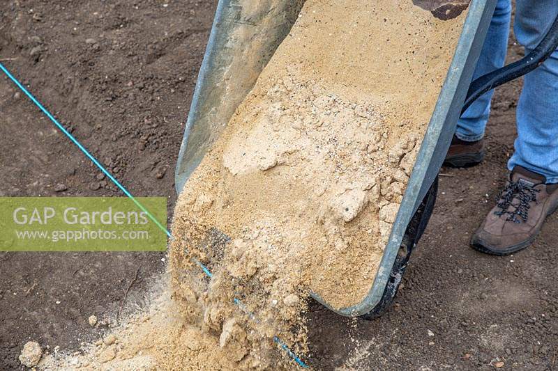 Adding gravel to base of path by tipping from wheelbarrow. 