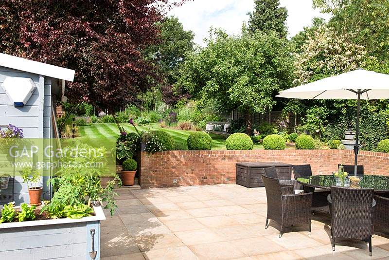 Patio area with dining furniture and umbrella - view to retaining wall and lawn