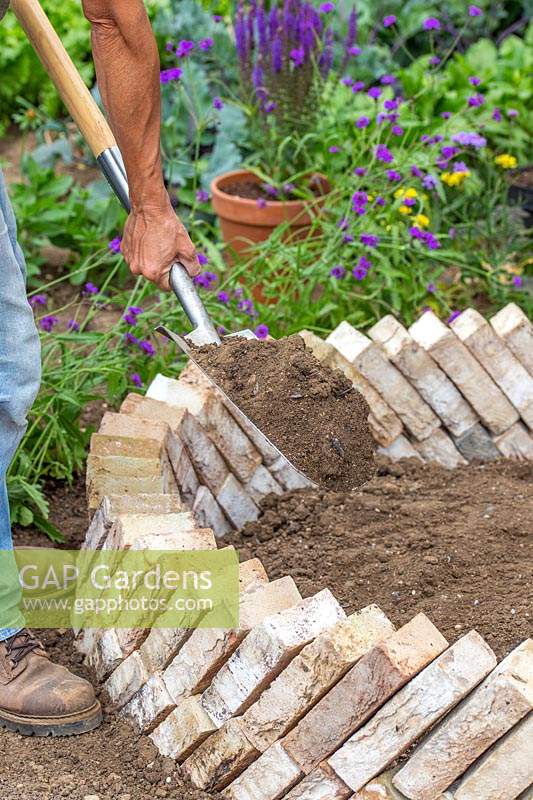 Woman adding well draining soil to raised bed