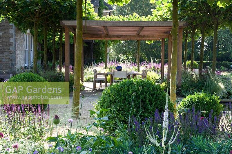 Wooden pergola and shaded dining area in modern garden, with clipped Box balls. 