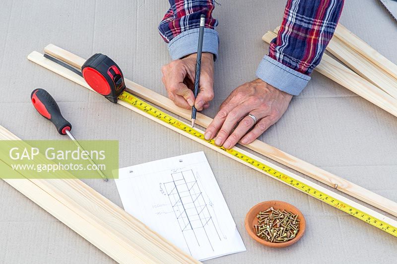 Woman measuring length of wooden strips with tape measure. 