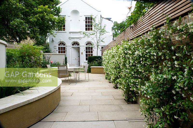 Modern, urban garden and house with pale paving and curved benching. 