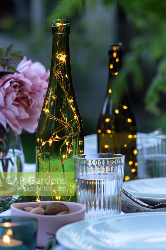 Fairylights in bottles create centrepieces on dining table in garden.
