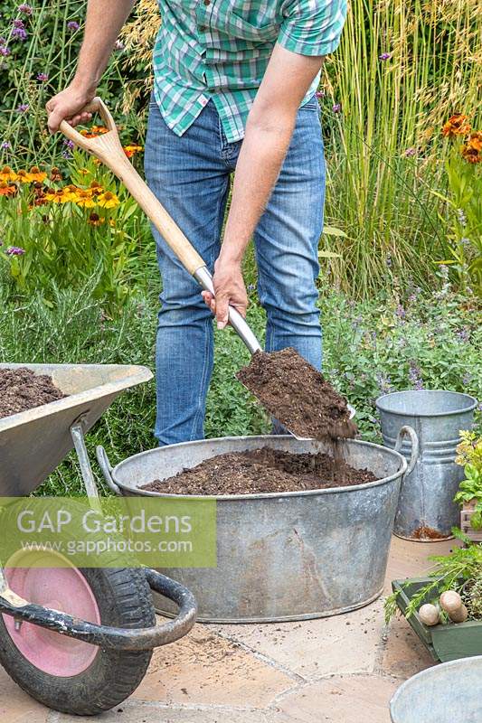 Man adding compost to the container using a spade. 