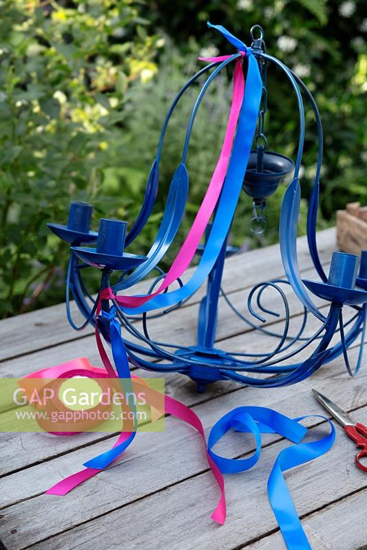 Cut lengths of brightly coloured ribbon and fasten on to the top of the sprayed chandelier, allowing the ribbon to drape. Leave a length once the ribbon is secured at the bottom so this will flutter in the breeze